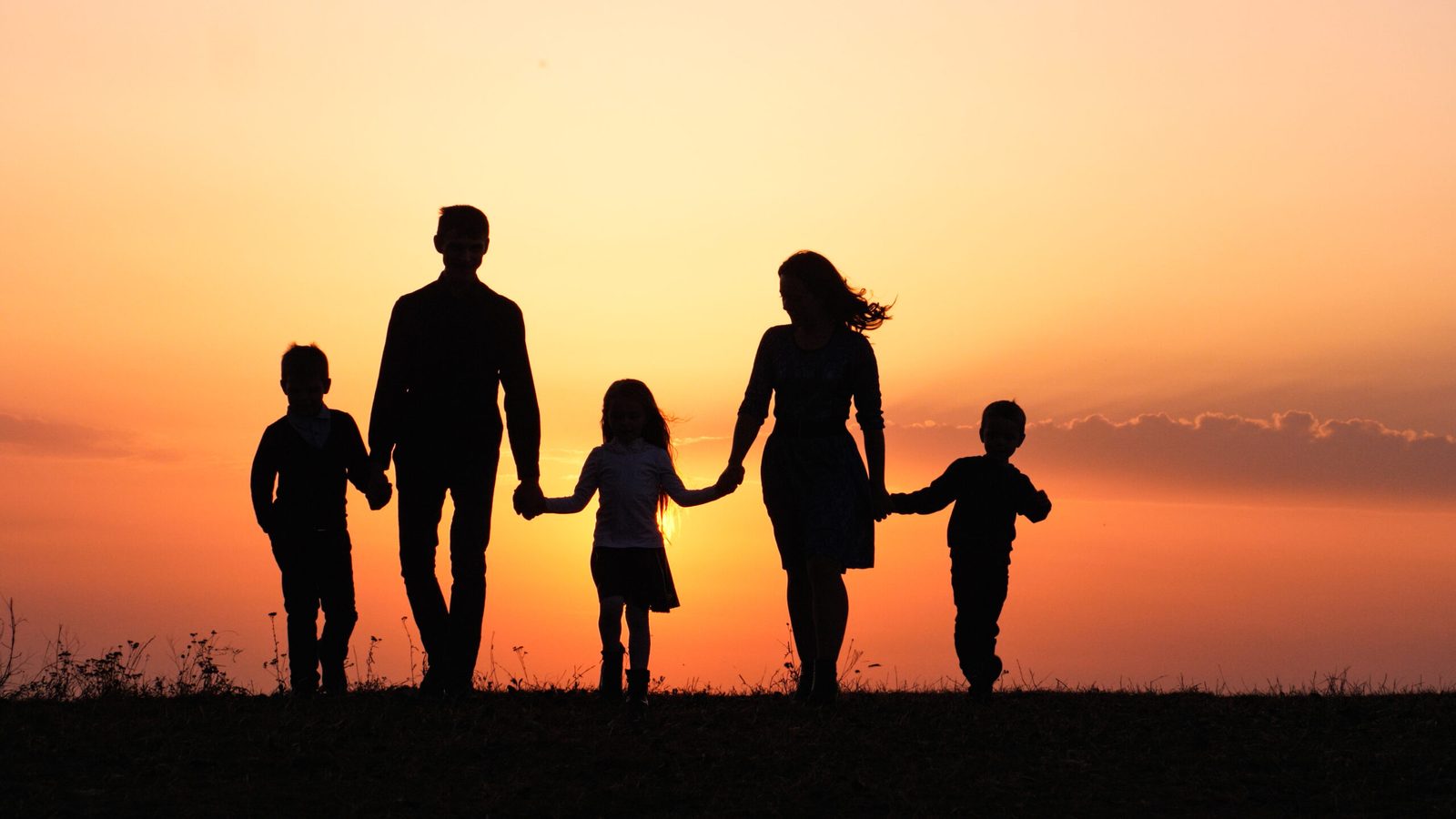 A family silhouetted against a sunset sky, holding hands
