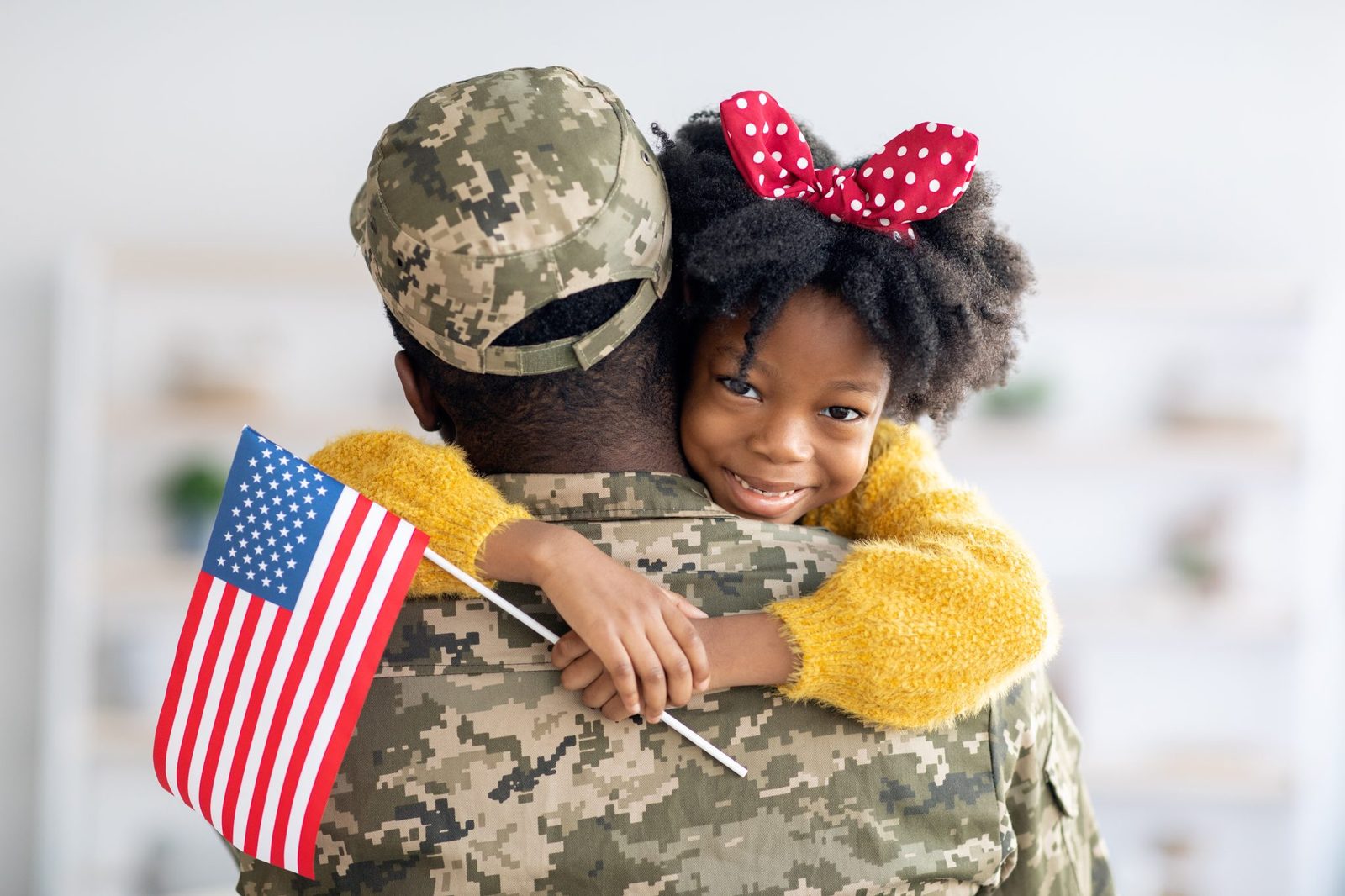 A service member embracing his daughter while she holds a small American flag